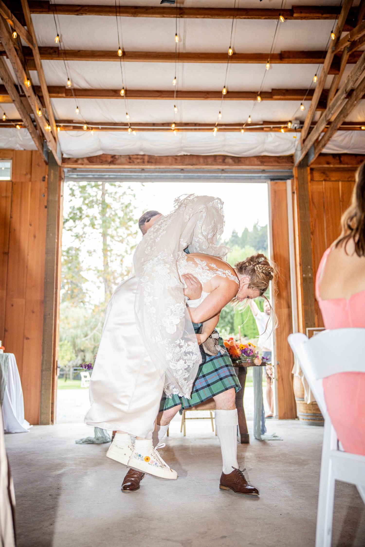 Dramatic wedding dip pose in rustic wooden venue with string lights overhead.