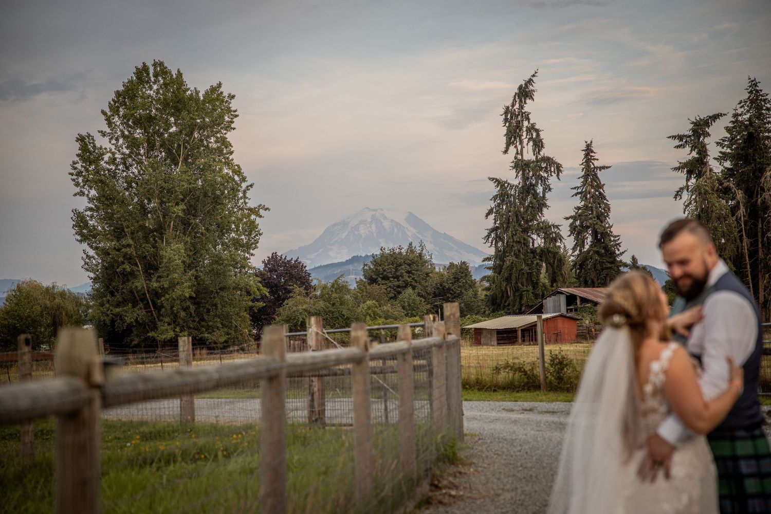 Scenic wedding portrait with mountain views and rustic wooden fence in background.
