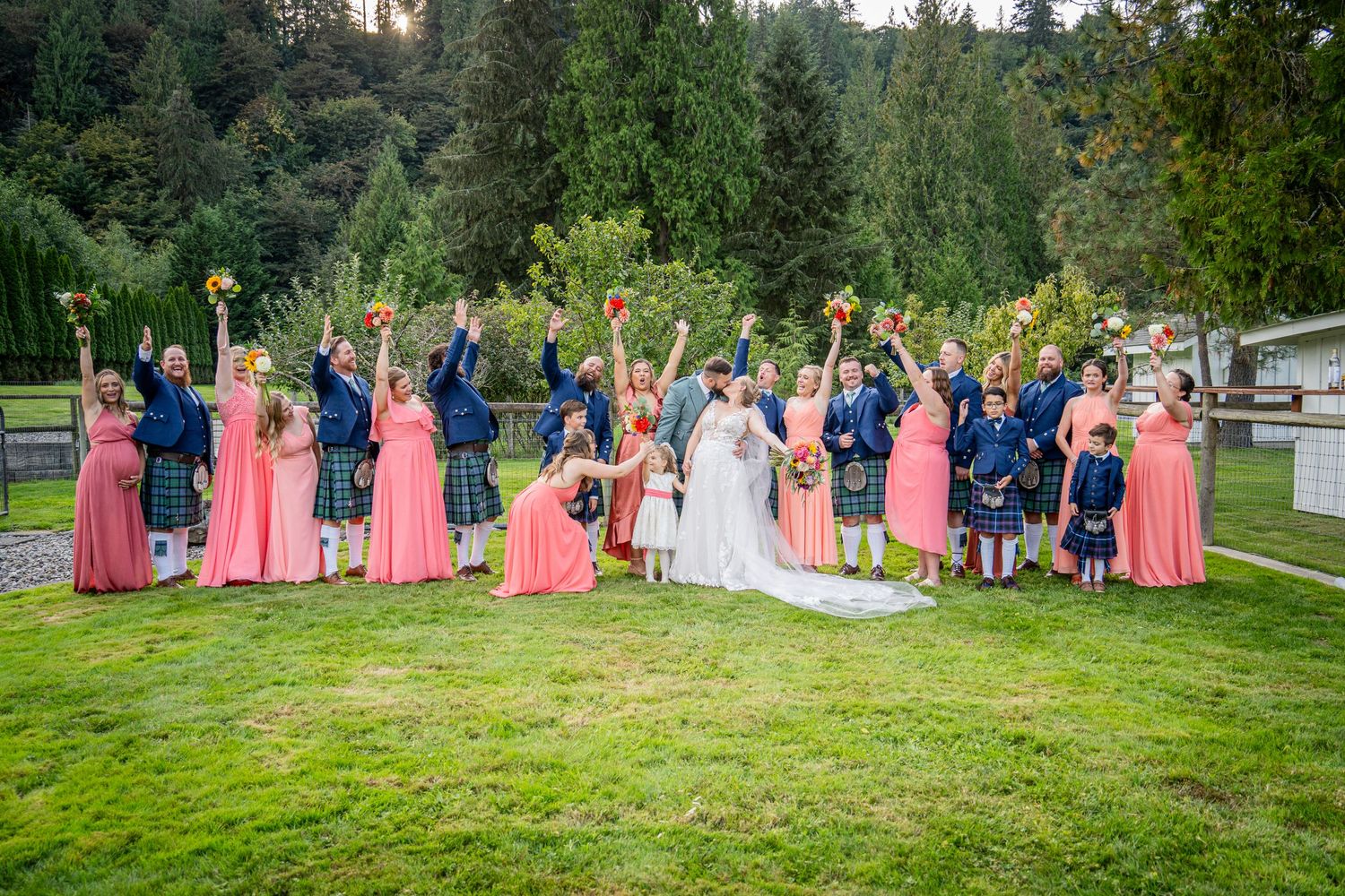 Wedding party in coral dresses and Scottish kilts celebrating on a lush green lawn.