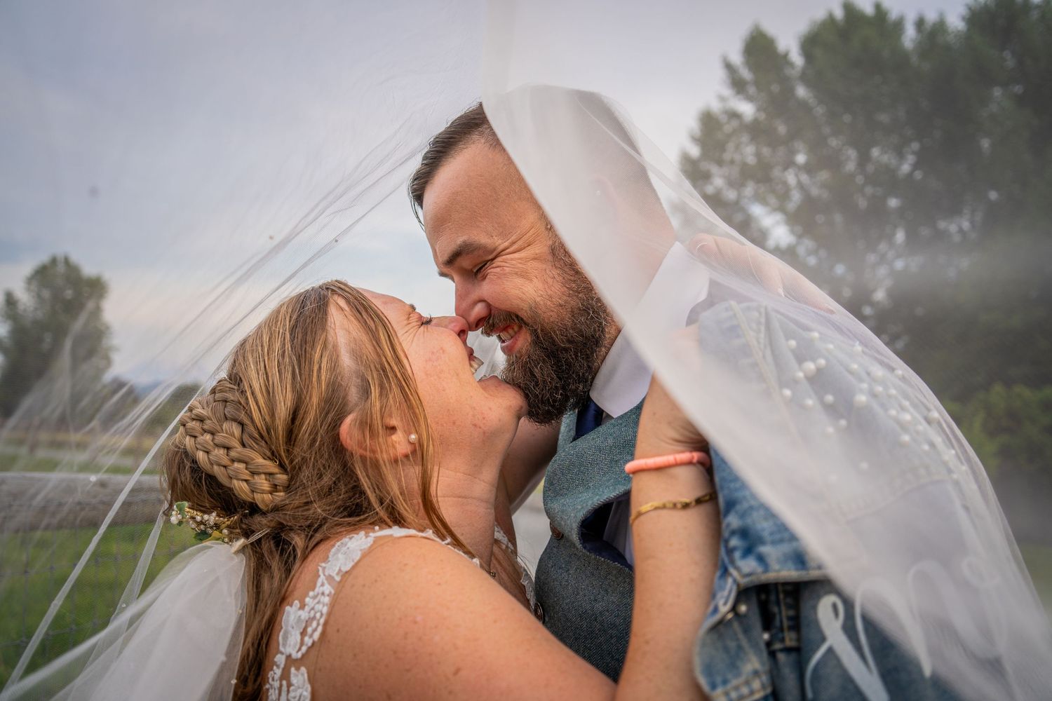 Romantic moment under a flowing veil during an outdoor wedding celebration.