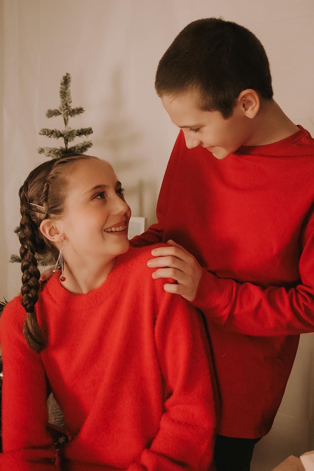 A romantic couple in matching red sweaters share tender moments in a series of intimate holiday photos by a Christmas tree.