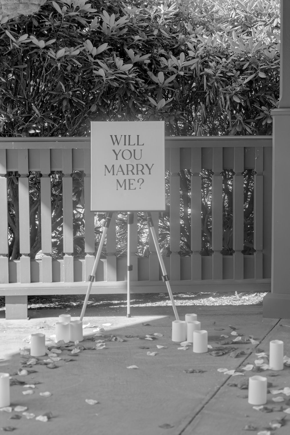 Creative marriage proposal setup with 'WILL YOU MARRY ME?' spelled out on white fence panels with tea lights on ground.