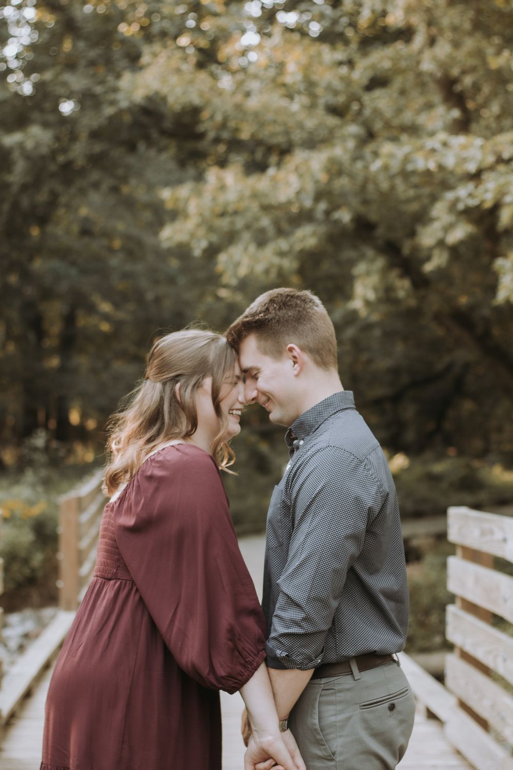 A couple shares intimate moments in a romantic outdoor photoshoot at a wooden bridge surrounded by fall foliage.