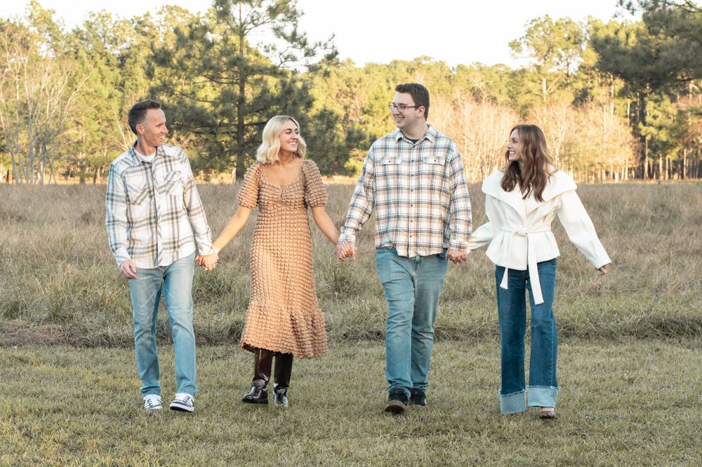 Four people hold hands while walking through a rustic field during golden hour.