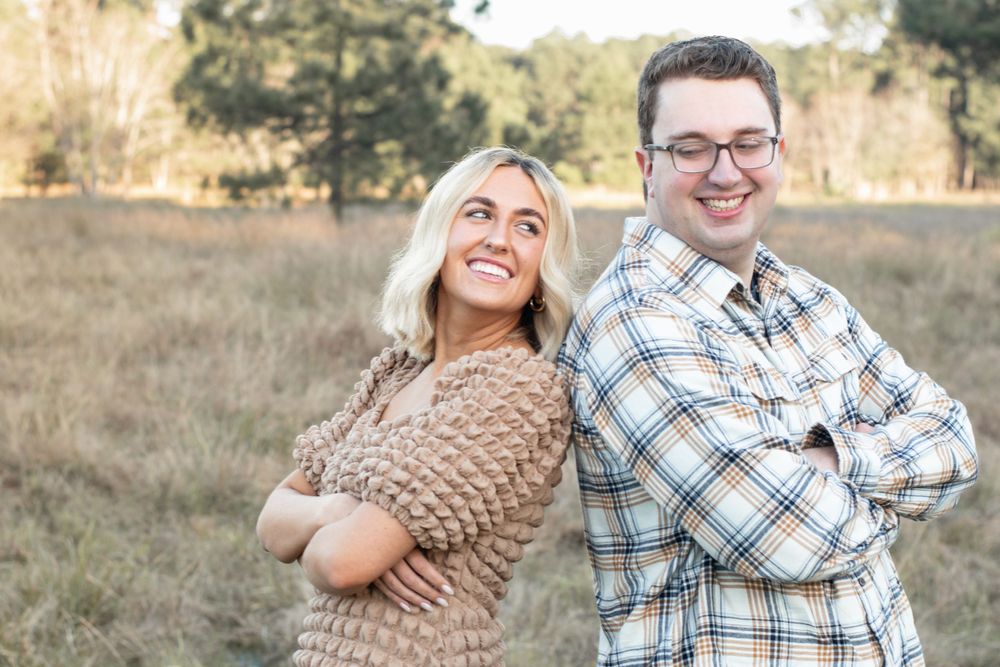Two people pose back-to-back in casual attire during an outdoor photo session.