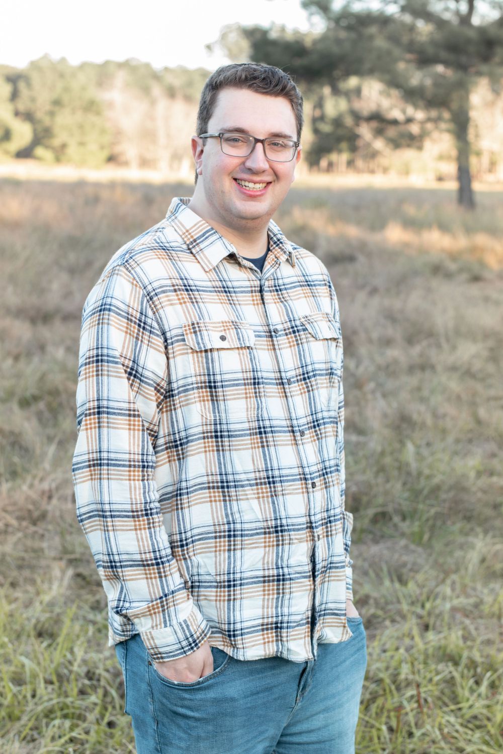 A person in glasses and plaid shirt smiles during an outdoor portrait session.