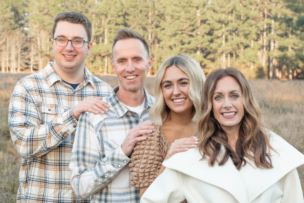 Four people smile together during a family photo session in a rustic field.