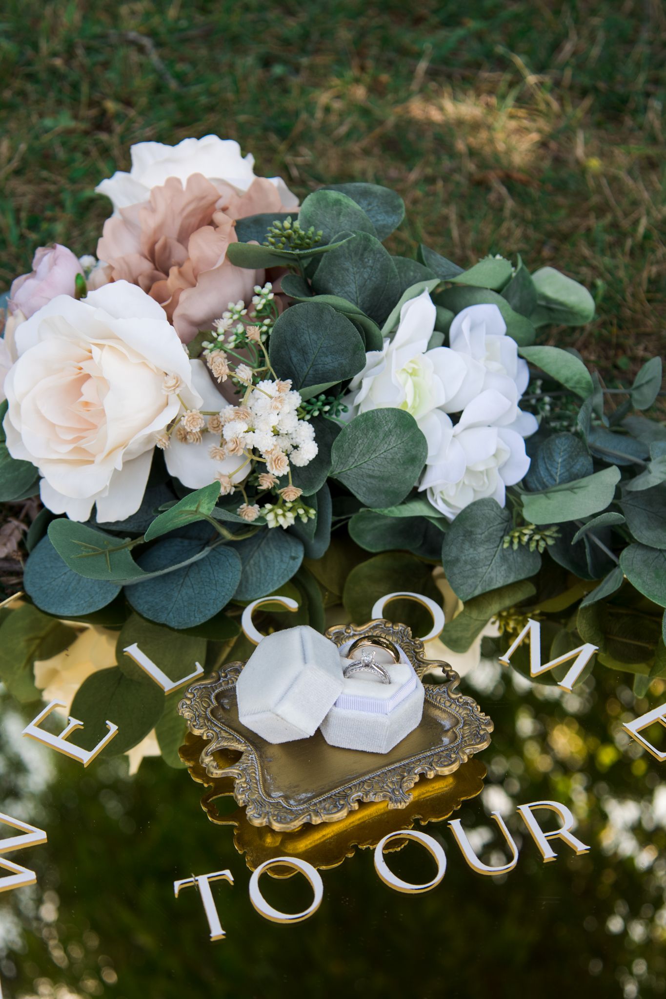 Wedding rings displayed on ornate tray with blush roses and eucalyptus floral arrangement.
