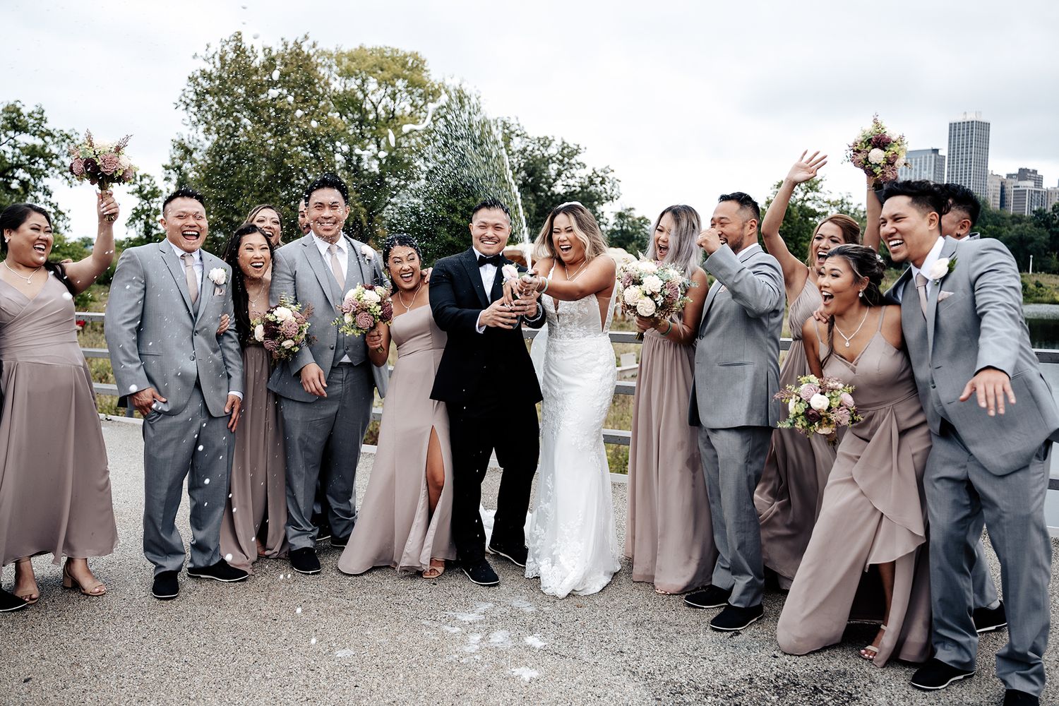 Wedding party celebrates outdoors wearing coordinated grey suits and blush bridesmaid dresses.