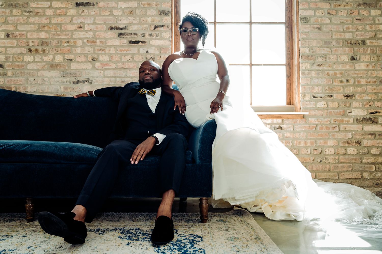 Newlyweds relax on a blue velvet couch against exposed brick walls.