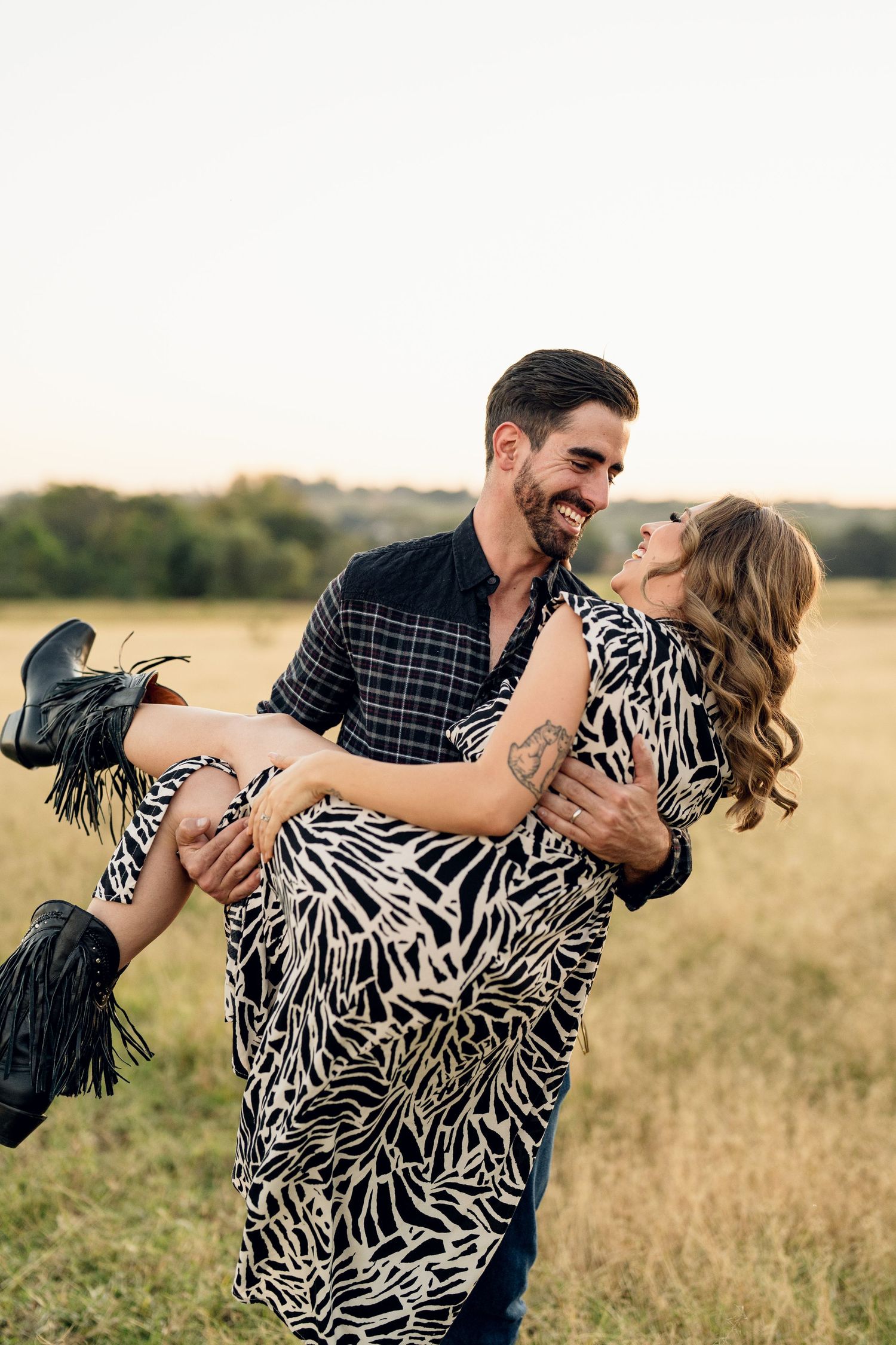 Playful couple dances in a golden wheat field during sunset photoshoot.
