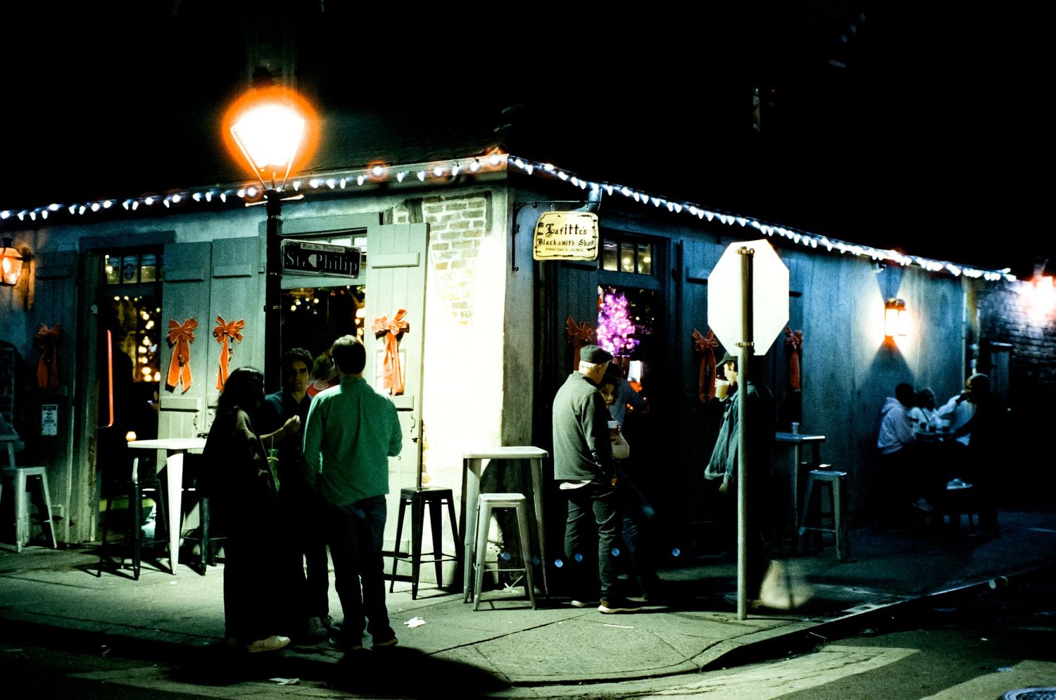 People socializing outside a small illuminated bar with string lights at night.