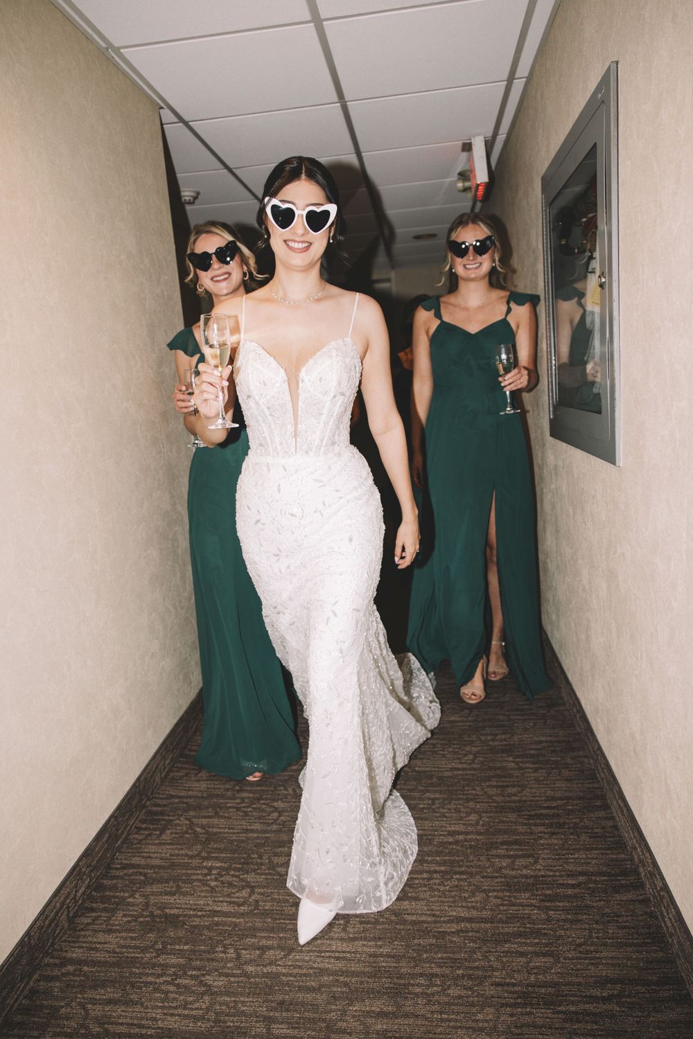 Wedding party walking down hallway wearing sunglasses and elegant dresses.