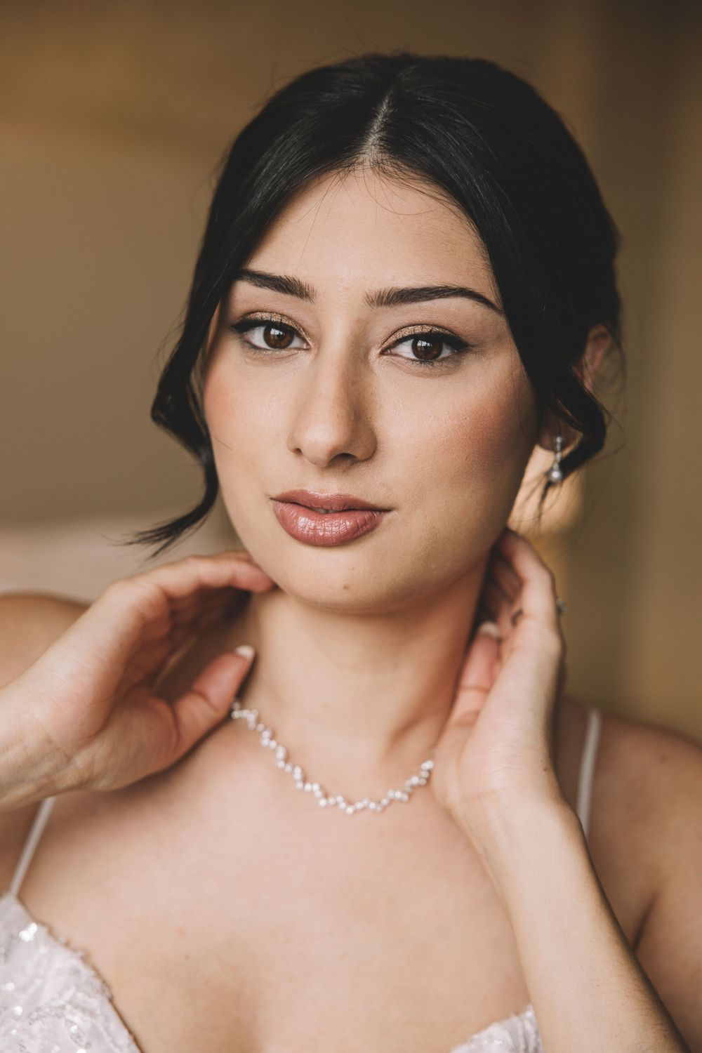 Elegant portrait of a bride wearing a delicate necklace and strapless gown in warm lighting.