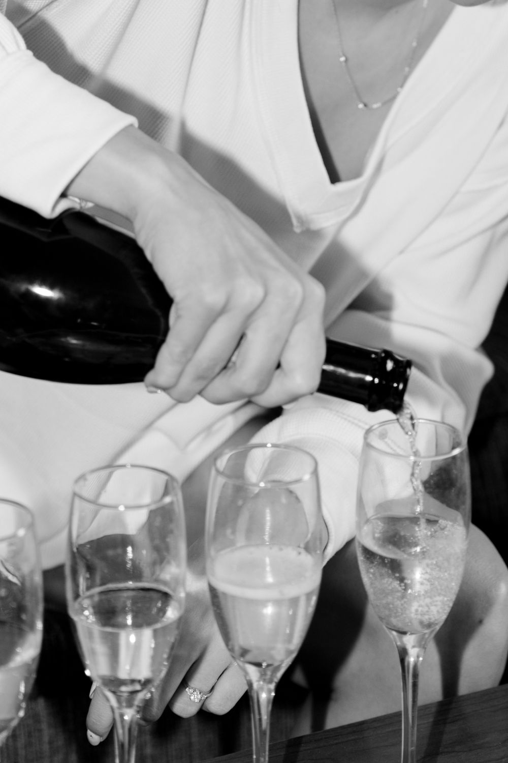Hands pouring champagne into multiple flute glasses in black and white.