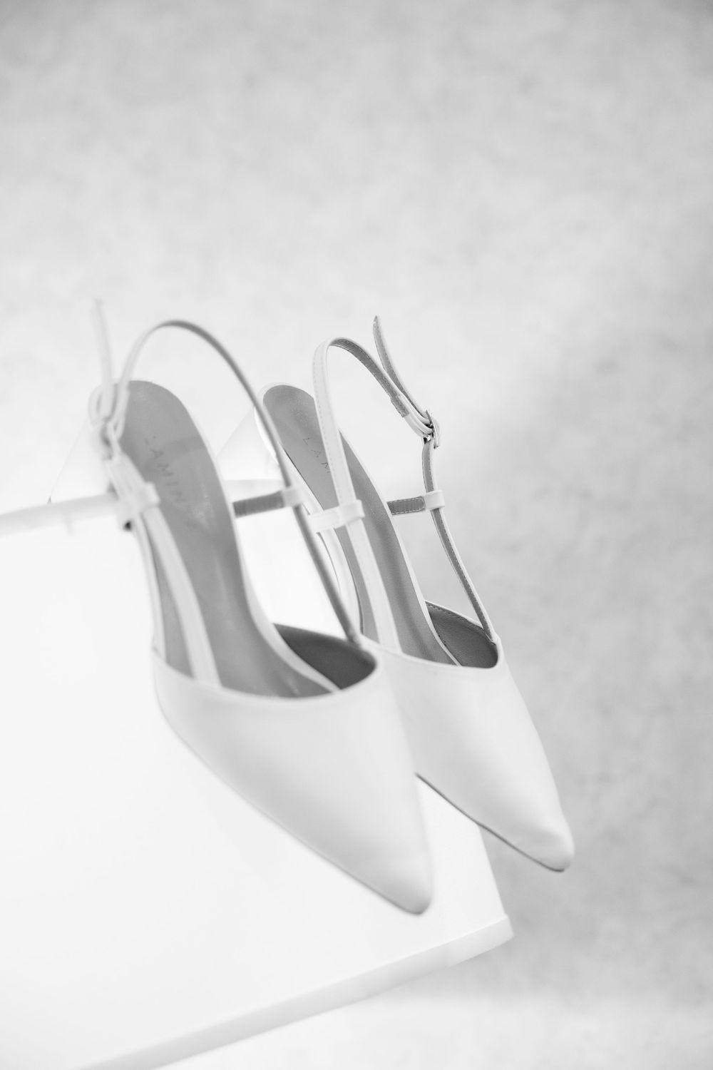 A pair of elegant white slingback high heel shoes photographed in black and white against a light background.