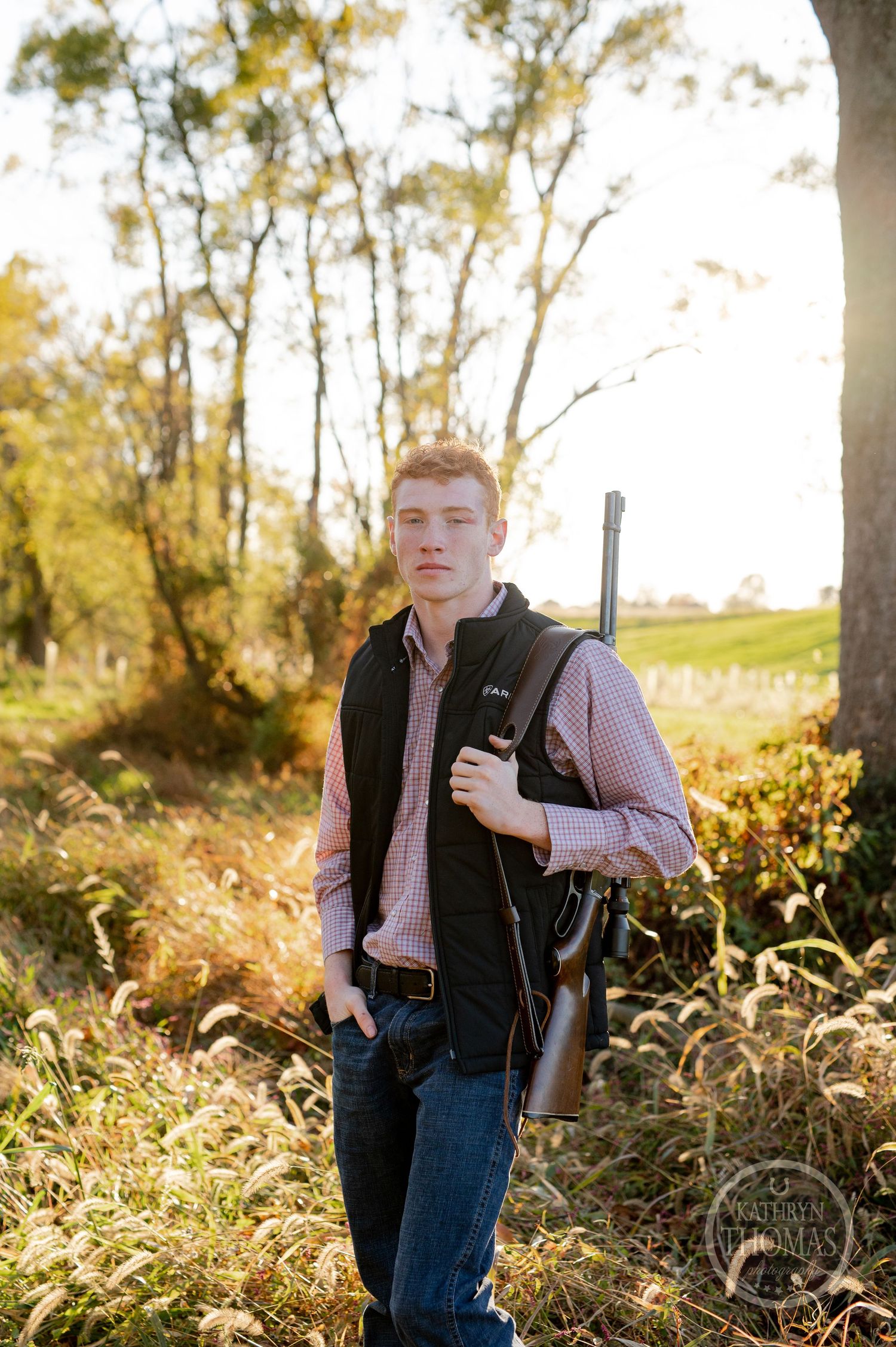 Someone holding a hunting rifle while standing in tall autumn grass.