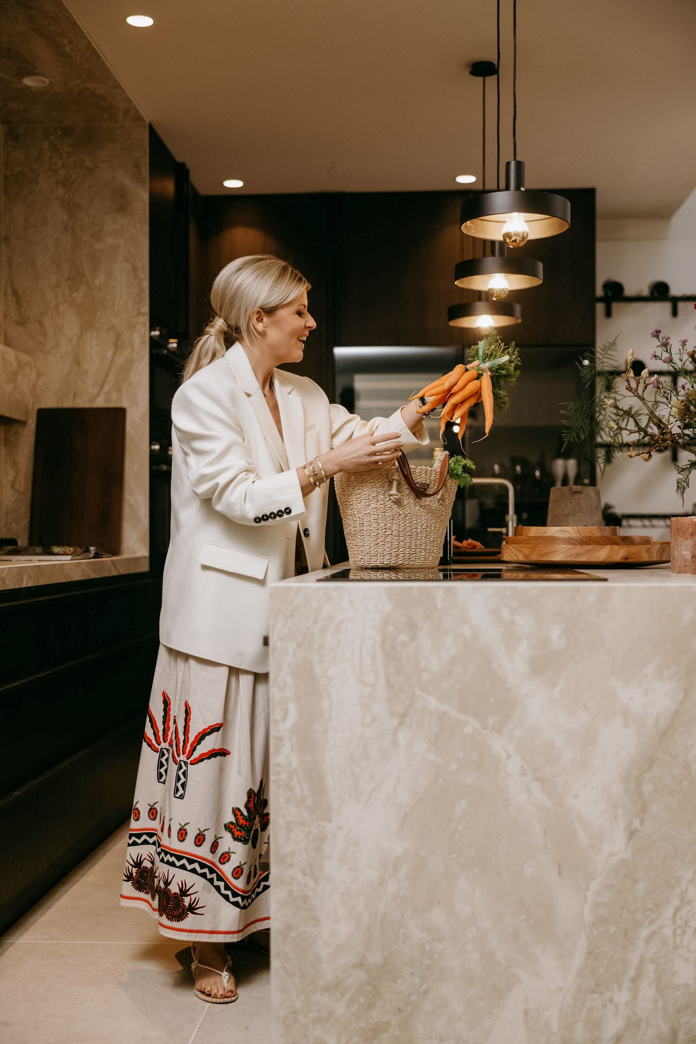 Person in white blazer and patterned skirt organizing produce in modern kitchen.
