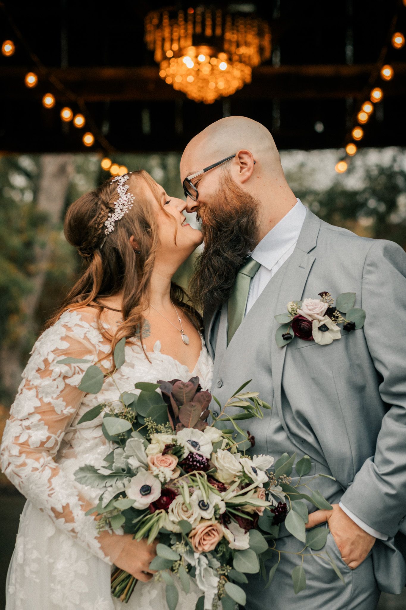 Romantic wedding couple sharing a kiss under a chandelier with the bride holding a lush floral bouquet. Pittsburgh wedding Photographer