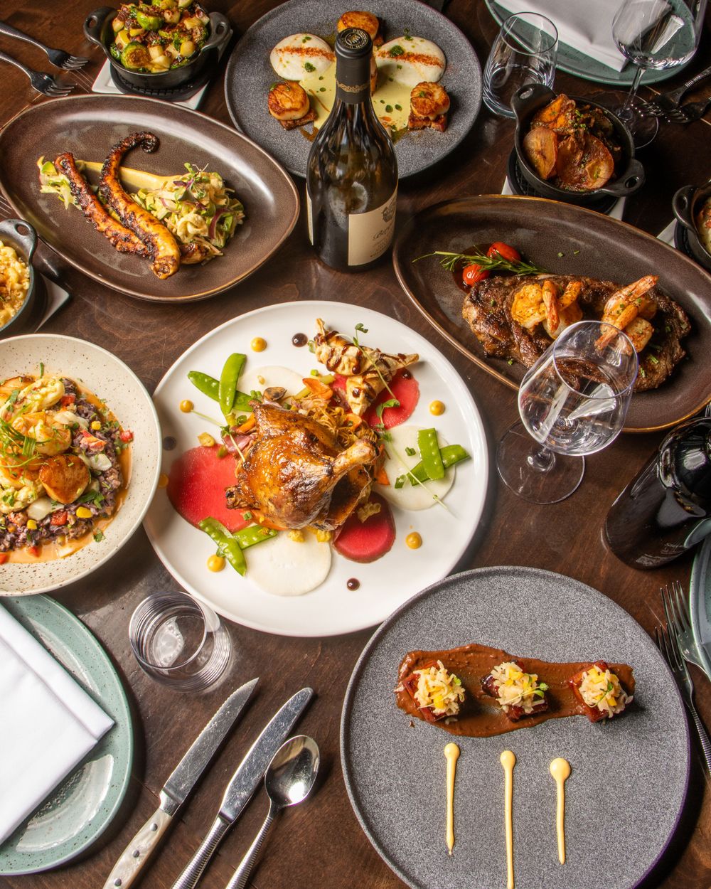 Elegantly plated gourmet dinner spread with multiple dishes and wine glasses on wooden table. By NJ Photographer Andrew Fein