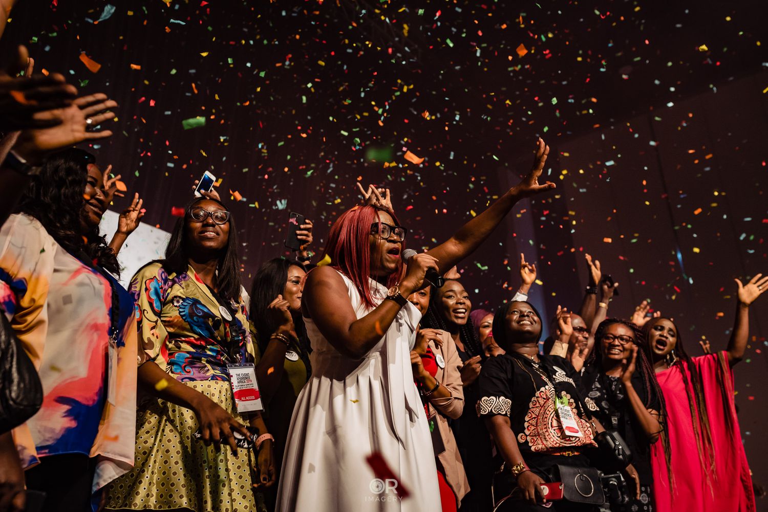 Crowd celebrating at a party with colorful confetti falling as people dance and cheer in festive atmosphere.
