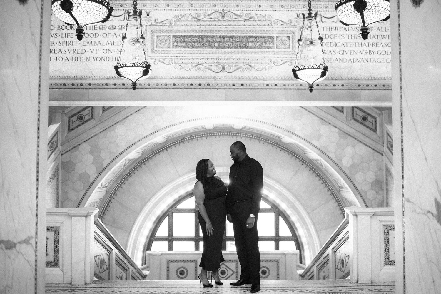 Two silhouetted figures stand beneath an ornate arched hallway with decorative ceiling and hanging light fixtures.