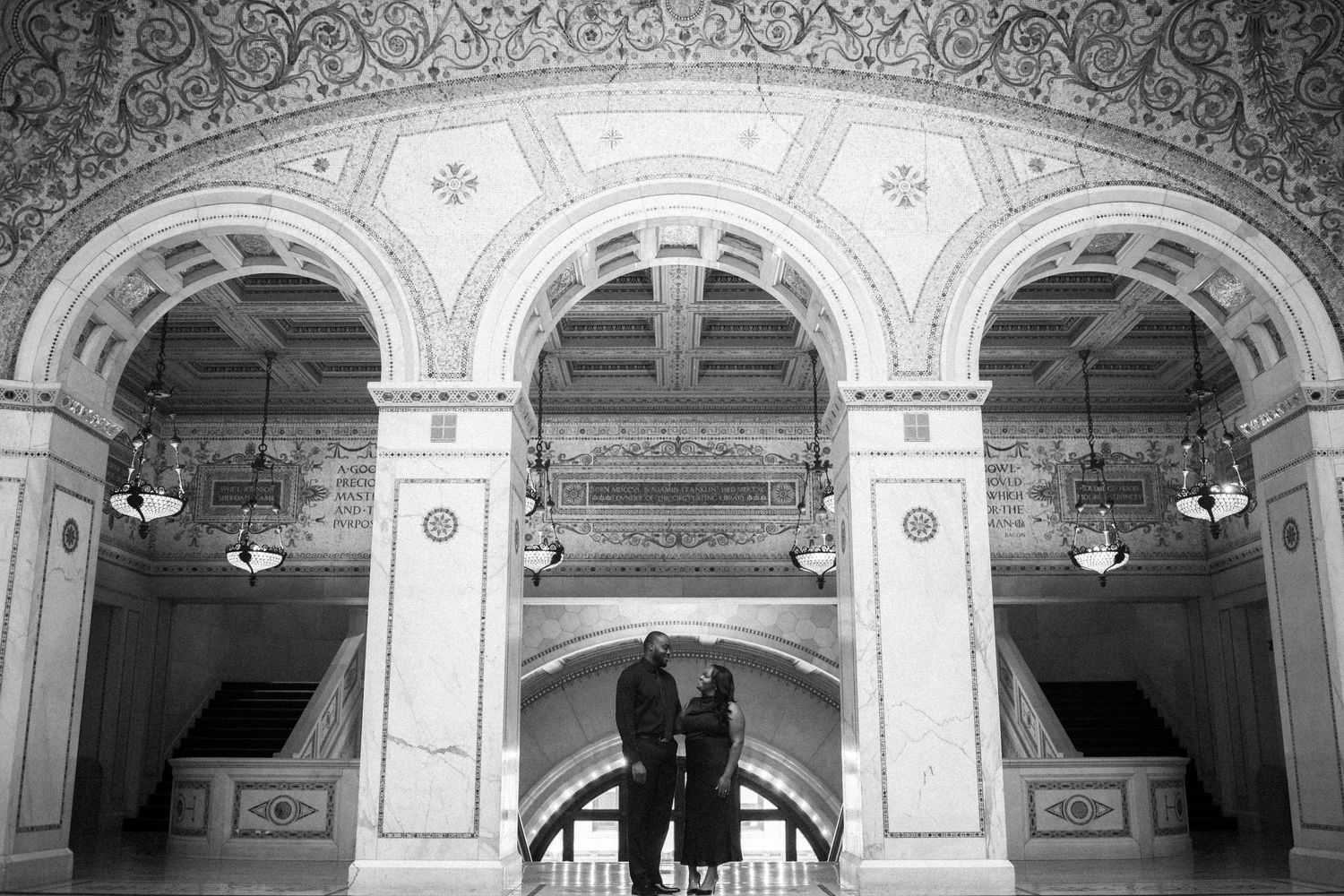 A couple dancing in silhouette beneath ornate arched architecture with classical details and hanging light fixtures.