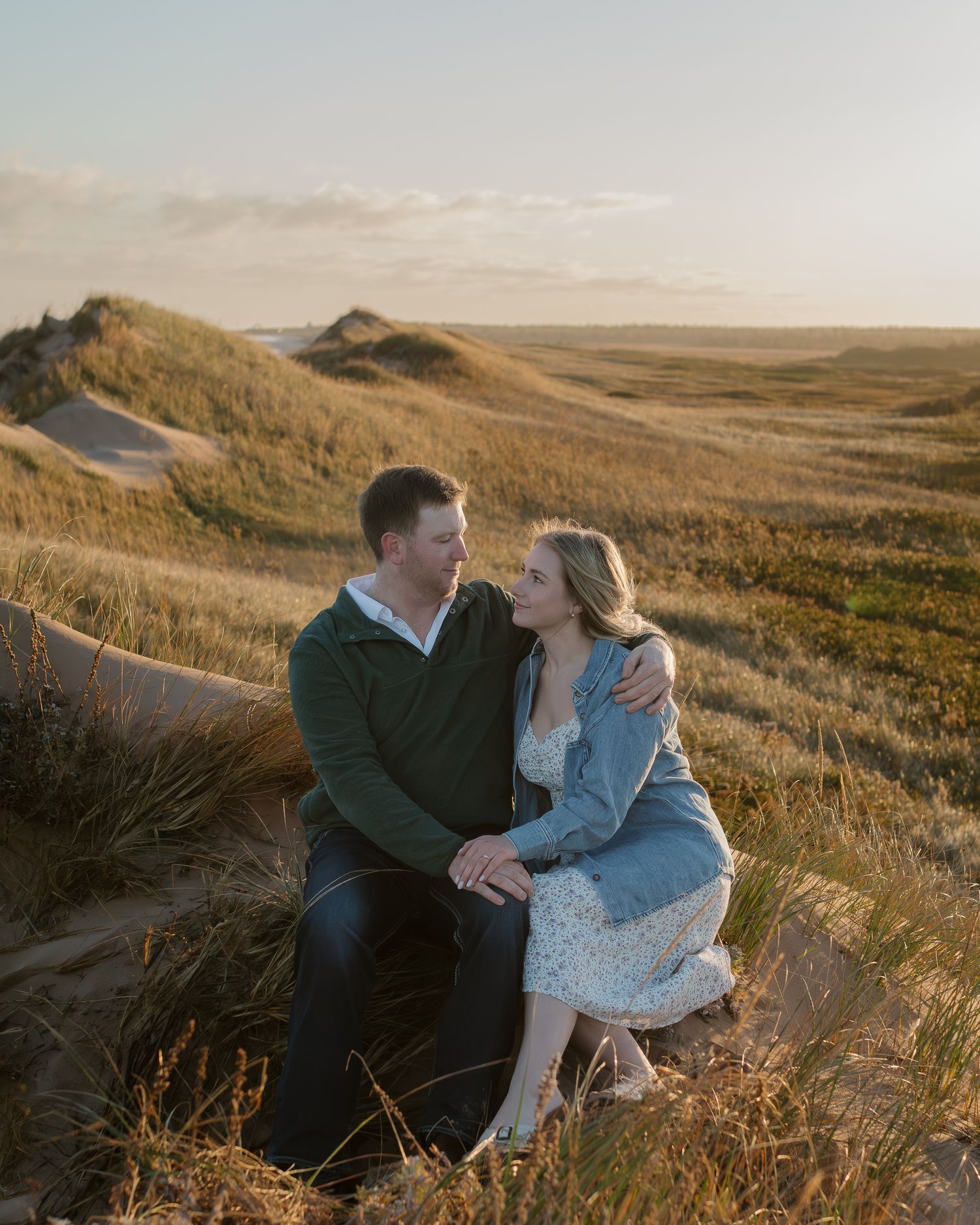 A romantic sunset engagement photo on grassy coastal cliffs.