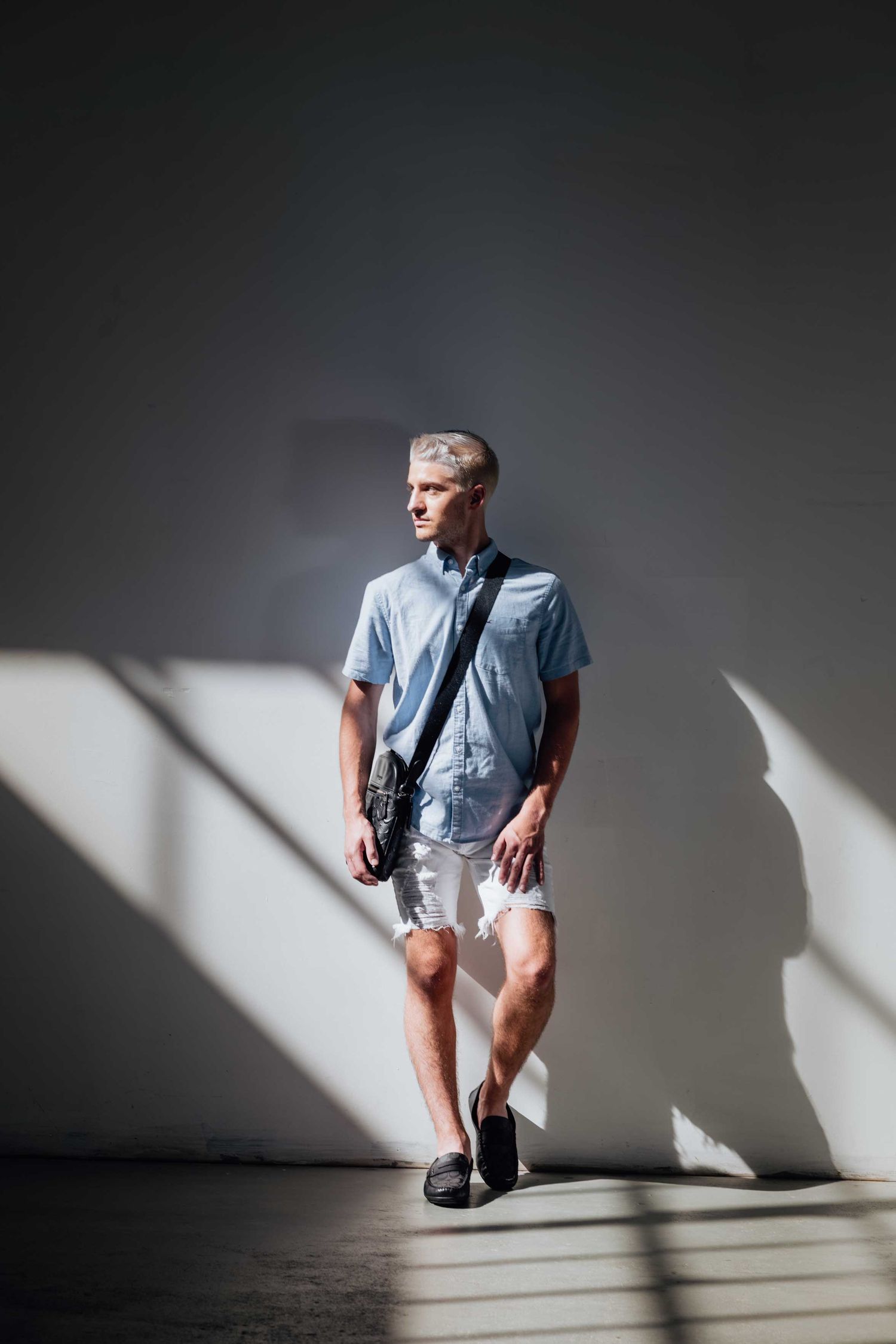 A fashion portrait of someone in casual summer wear standing in dramatic window light.