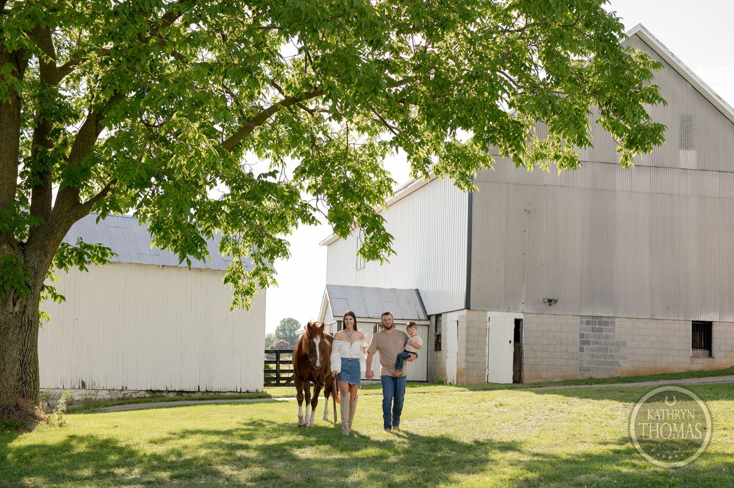 Family walking together on sunny farm grounds near a large white barn.