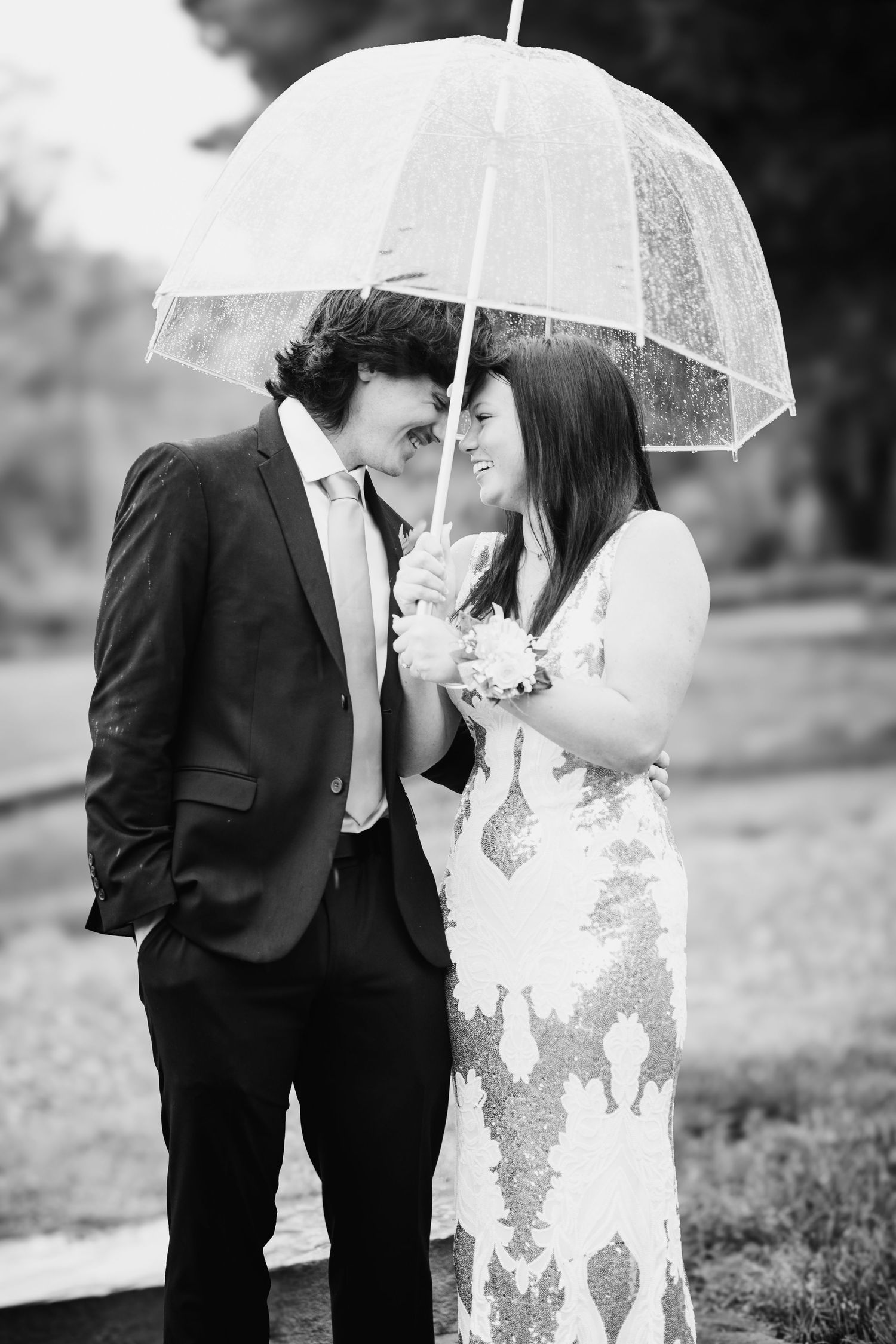 Romantic black and white photo of couple sharing intimate moment under clear umbrella.