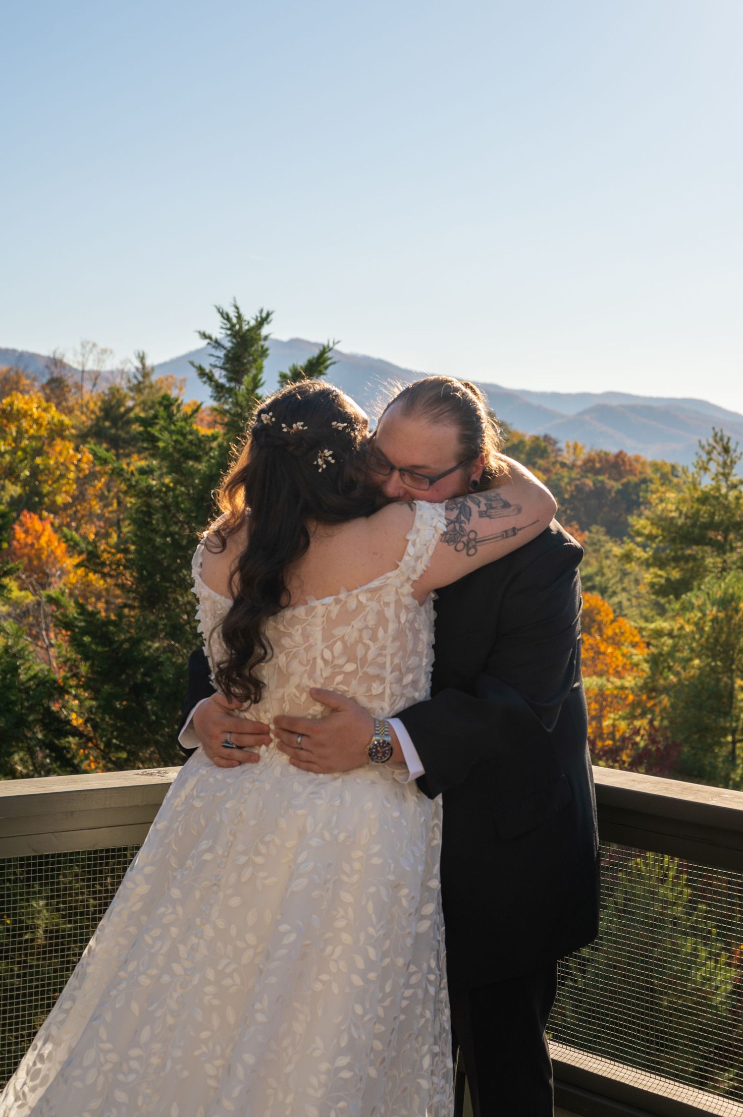 Newlyweds share an intimate embrace on a mountain deck surrounded by fall foliage.