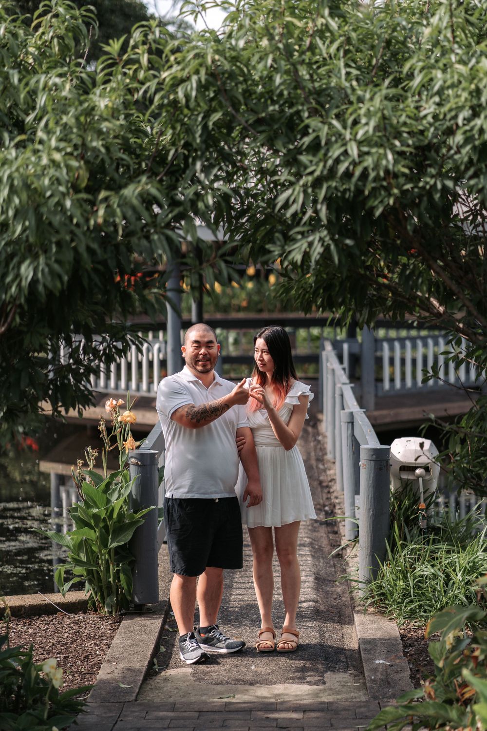 A couple shares a tender moment on a wooden bridge surrounded by lush greenery in a garden setting.