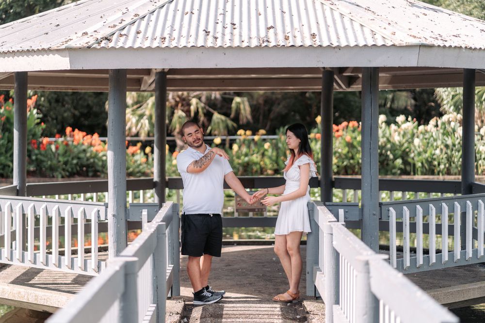 A couple shares a playful moment under a covered pavilion surrounded by flowers.