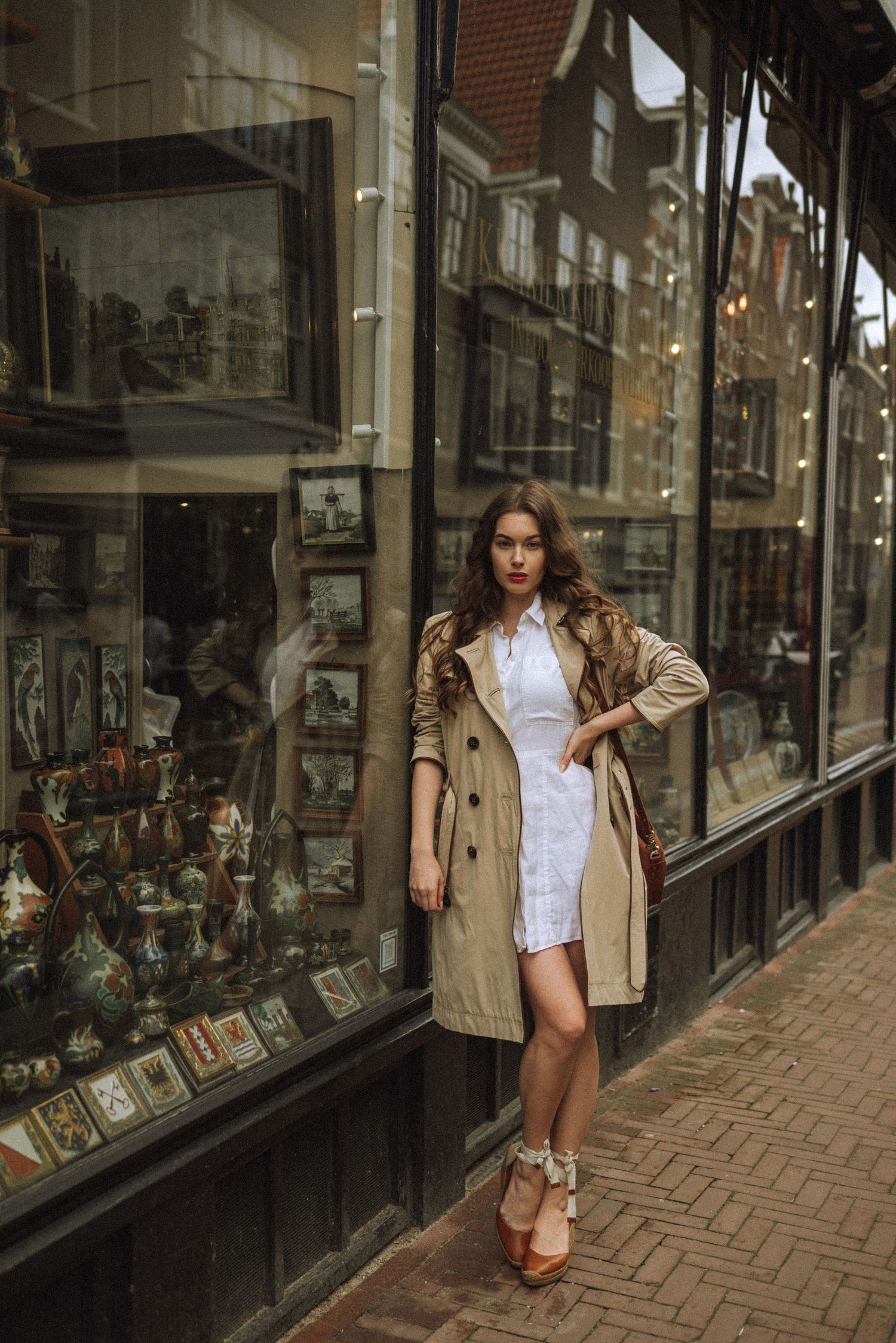A woman gazing into the camera during an individual portrait session in Amsterdam, standing near the window of a famous antique shop.