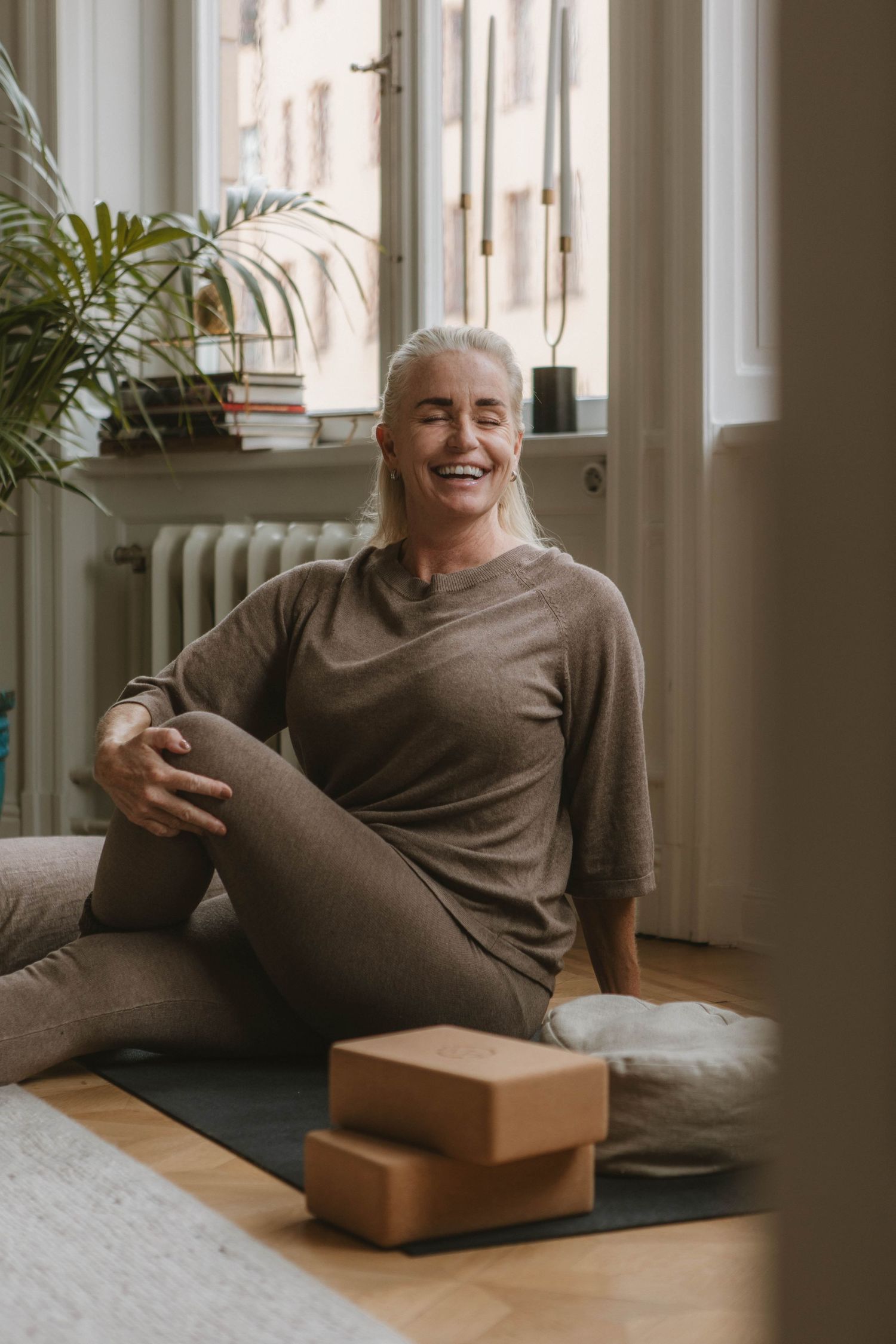 Person relaxing on floor at home with yoga blocks and houseplant by sunlit window.