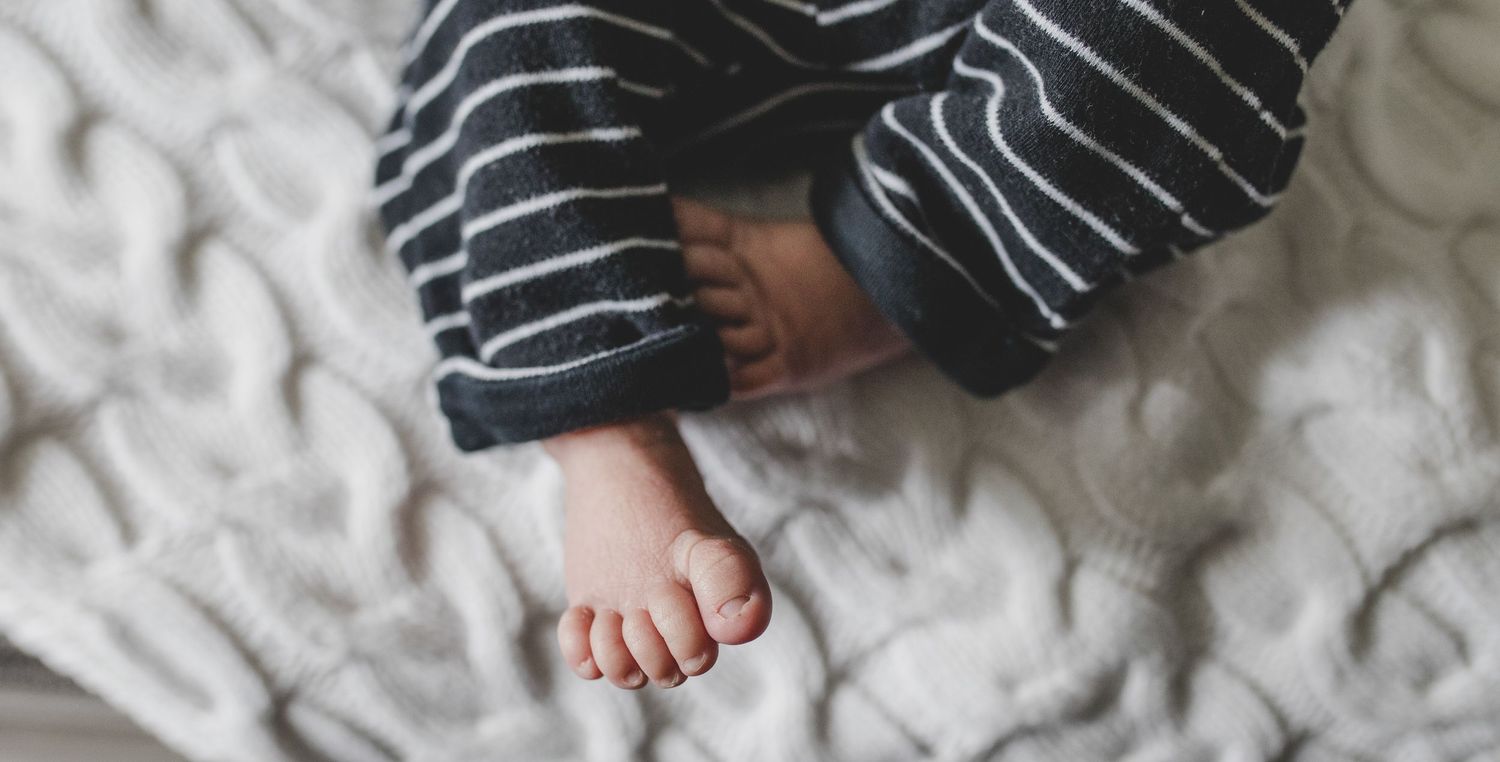 Small bare feet peeking out from under striped clothing on white textured bedding.