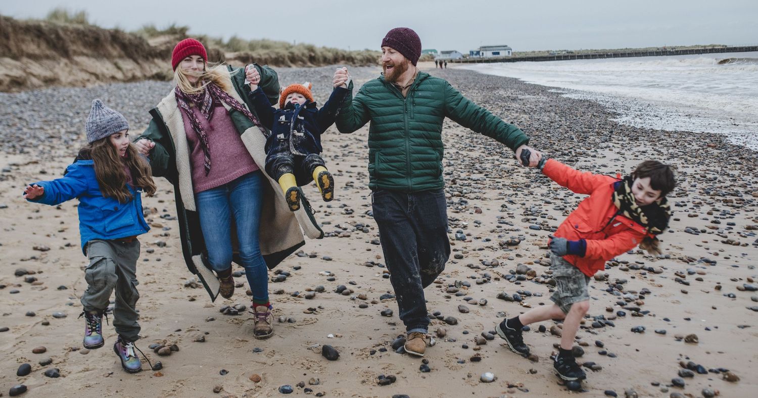 Family playing and jumping together on rocky beach shore.