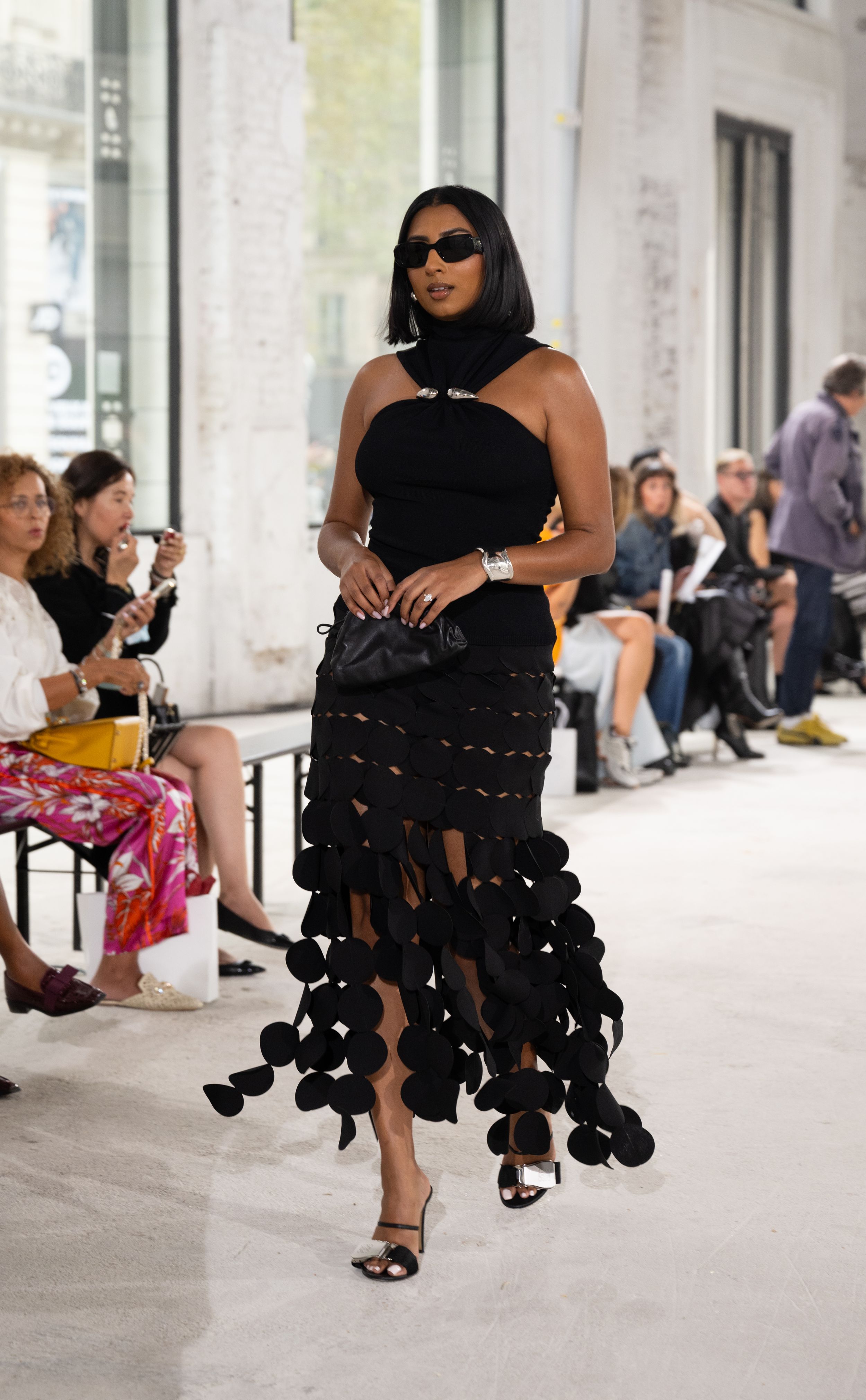Black halter dress with dramatic pom-pom fringe detail and sunglasses at fashion show.