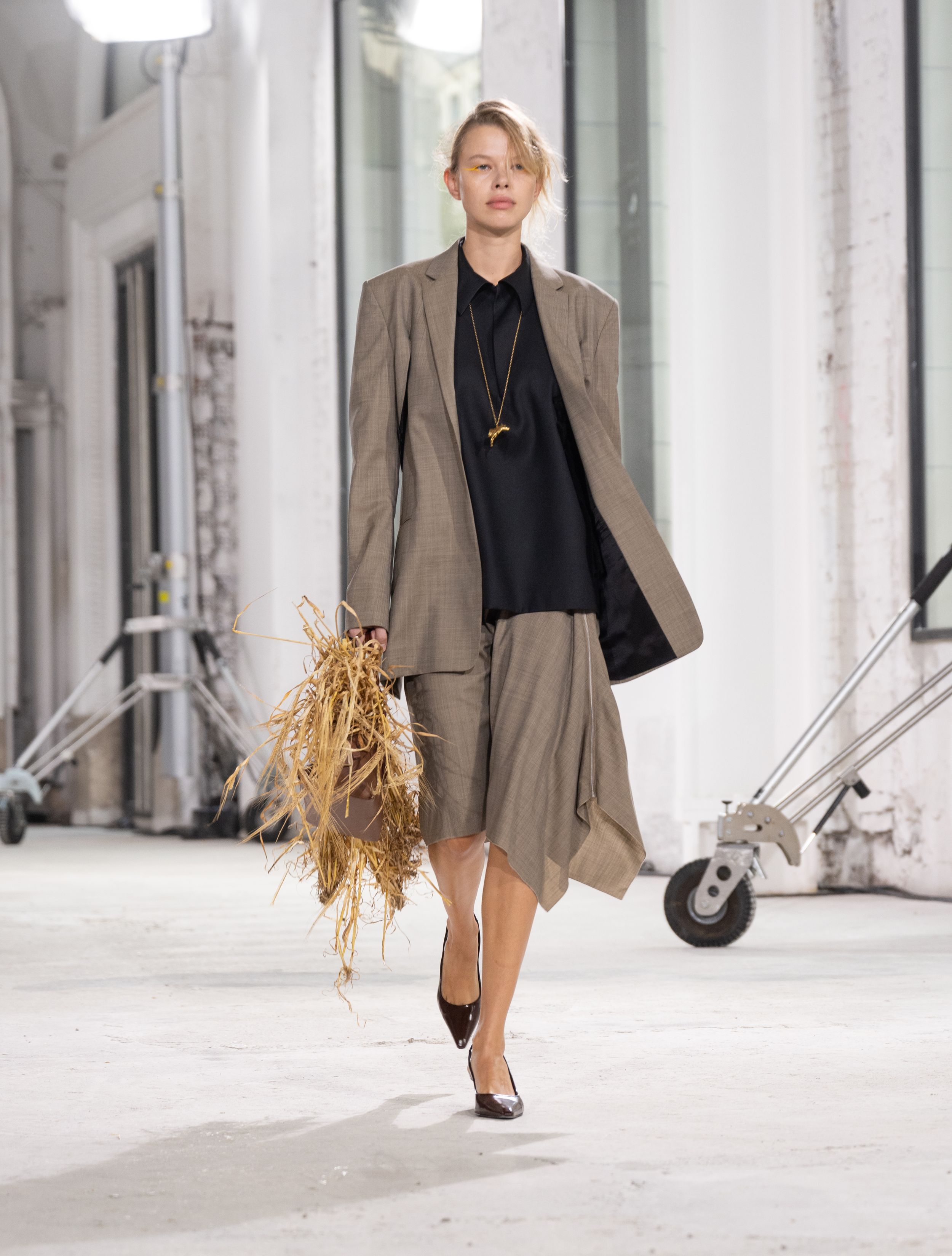 Tailored beige blazer and flowing skirt ensemble accessorized with dried wheat stalks.