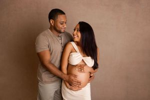 Intimate maternity photo of couple embracing against beige background as they await their baby's arrival. Maternity & Newborn Photographer