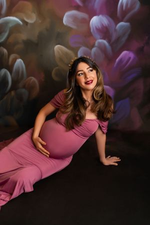 Stylish maternity photo with a pink dress against a dark background with soft bokeh floral effects. Maternity & Newborn Photographer in NJ