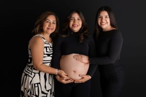 A maternity photo shows three women in black and white outfits posing together against a dark background. Morris County Studio Maternity Pho