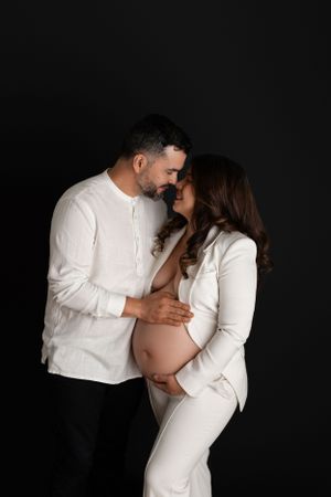 An expecting couple in matching white outfits share an intimate moment. Morris County Studio Maternity Photographer