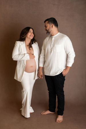 Expecting couple in matching white outfits share a tender moment during maternity photoshoot. Morris County Studio Maternity Photographer