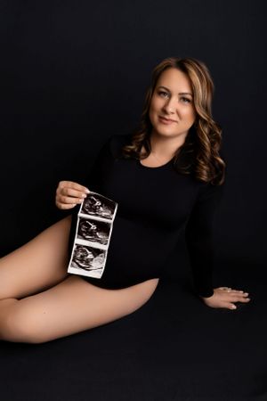 Artistic maternity photo black background featuring ultrasound photos while wearing a black bodysuit in Northern NJ Maternity Photographer