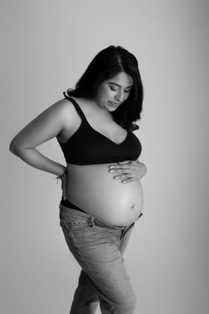 Black and white maternity photo of woman in tank top and jeans touching her pregnant belly. Studio Maternity Session in Sussex County NJ