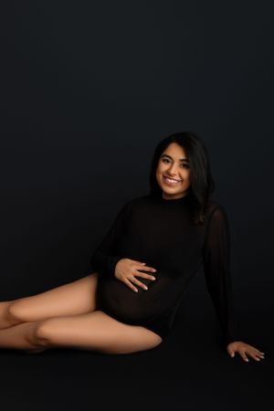 Portrait of woman in black turtleneck sweater lying gracefully against dark background. Studio Maternity Session in NJ photography studio