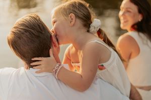 A child in white whispers a secret to someone during a sun-lit outdoor moment.