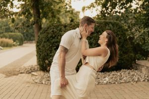 A romantic couple dances together on a stone pathway during golden hour with lush greenery in the background.